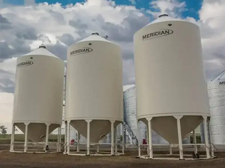 Large white fertilizer storage bins on a Canadian farm under a cloudy sky